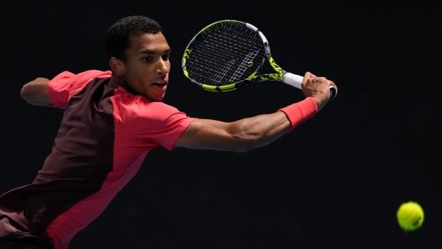 A male tennis player plays a backhand return.