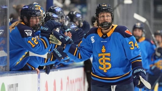 A women's hockey player gets a high-five as she skates by her teammates on the bench.