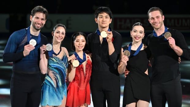 Six figure skaters hold up their medals as they pose for photographs.