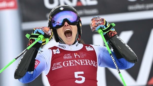 A female alpine skier shouts while raising her skis in celebration.