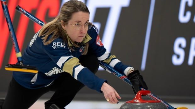 Female curler kneels down to throw rock with a broom held in hand