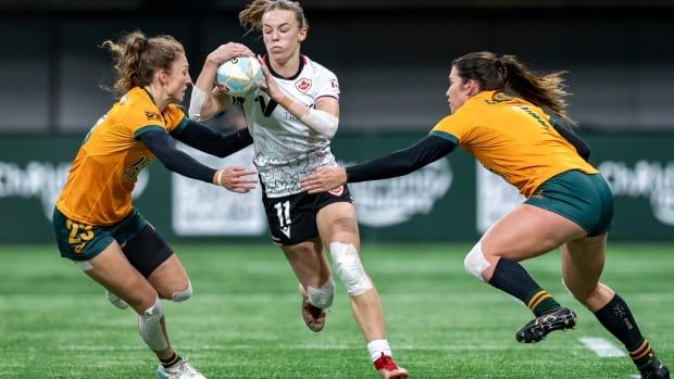 Female rugby player runs between two defenders with ball.