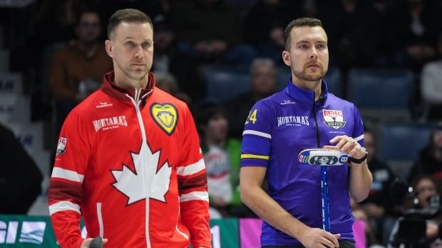 Two curlers stand on the ice.