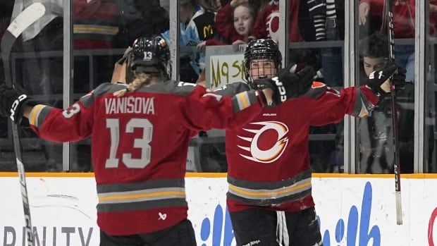 Two women's hockey players raise their arms in celebration.