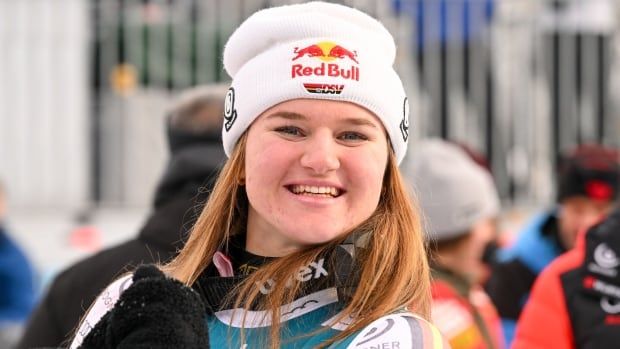 A women's alpine skier, wearing a white tuque, smiles.