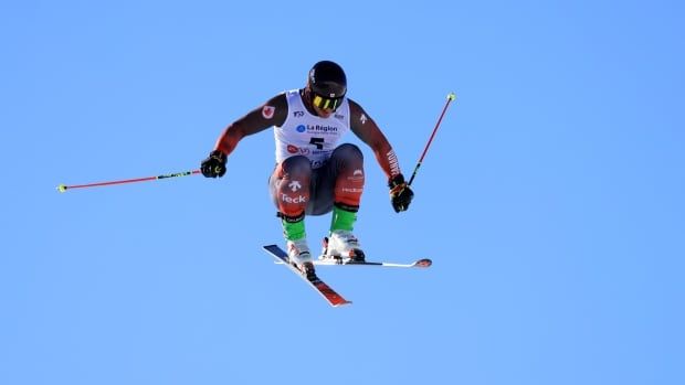 A male ski cross racer soars through the air during a daytime training session.