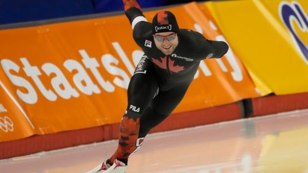 A male long track speed skater representing Canada speeds around an oval.