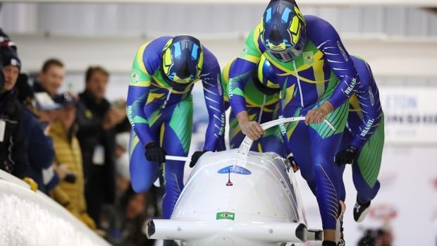 Four male bobsleigh athletes push their sled at the start of the race course