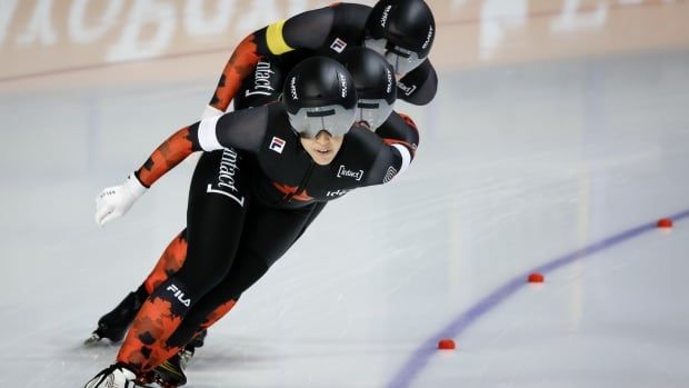 Three female speed skaters, round corner on track, tightly packed, one behind the other.