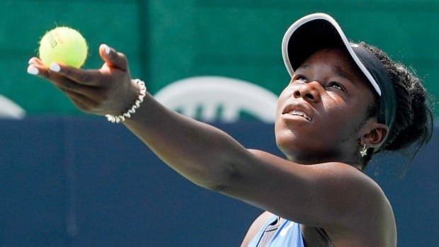 Female tennis player stretches arm out with tennis ball placed in hand to serve over the net.