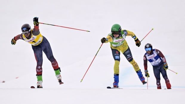 Three male ski cross athletes stretch out towards the finish line.