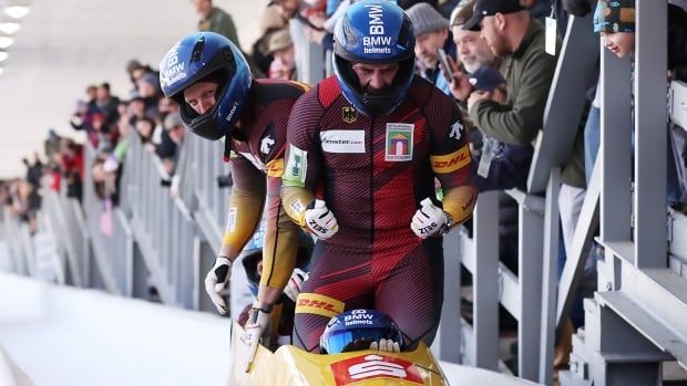 A four-man bobsleigh team celebrates a win, with one member pumping both fists as the crowd watches behind the track barrier.