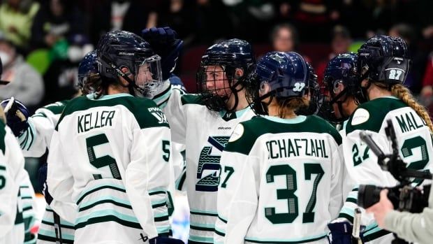 A group of women's hockey players wrap their arms around each other in celebration during a game.