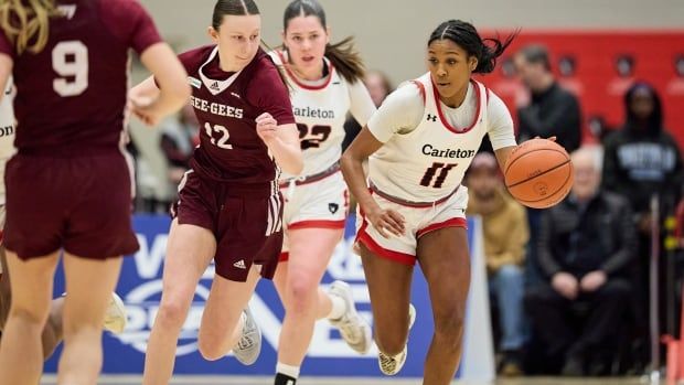 A female basketball player runs down the court while dribbling the ball with her left hand as an opponent pursues her.