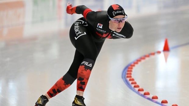 A female long track speed skater rounds a corner during a race.