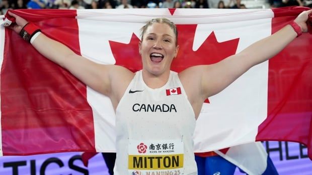 Female shot put athlete holds out stretched Canadian flag behind her in celebration.