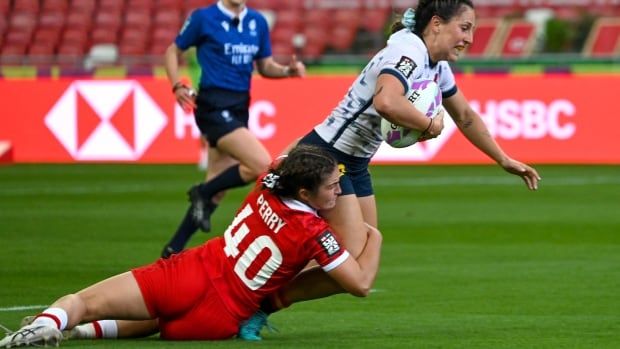 One female rugby player tackles her opponent around the legs, as she holds on to the ball.