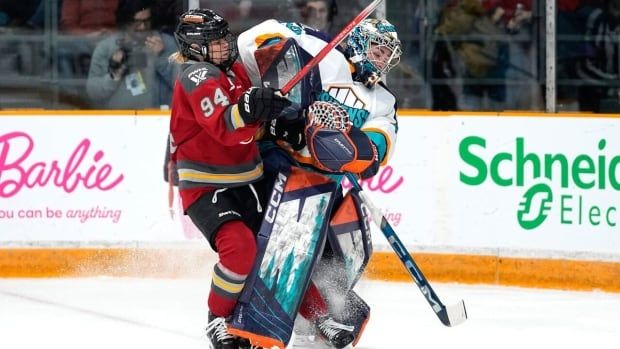 A female hockey goaltender battles for position with an opposing player.