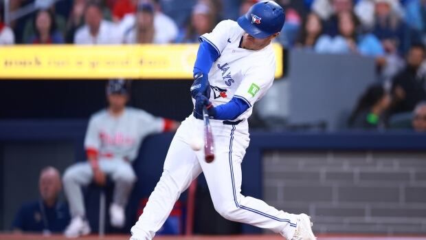 Male baseball player stands over plate, and rotates his body, swinging the bat to hit baseball.