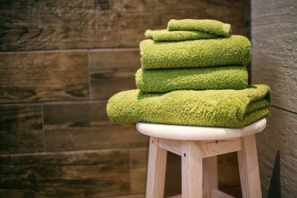 Three lime green towels and two washcloths stacked on a wooden stool.