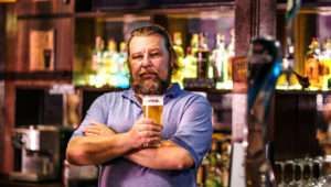 Man stood at the bar in a pub, pint in hand.