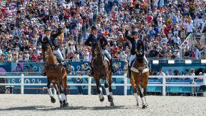 Ros Canter, Tom McEwen and Laura Collett celebrate their team gold medal during a laop of honour on their horses in front of the Paris 2024 crowds.