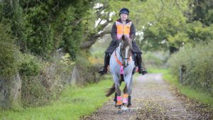 A horse and rider wearing high vis hacking down a track in the countryside towards the camera.