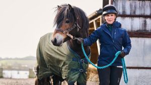 A lady leading hairy native pony wearing a turnout rug