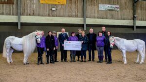 Ponies Alby and Spider look on with some of Unicorn Centre’s supported volunteers as (from left) Edmund Levie on behalf of Ferrum Lodge presents the cheque to chair of trustees