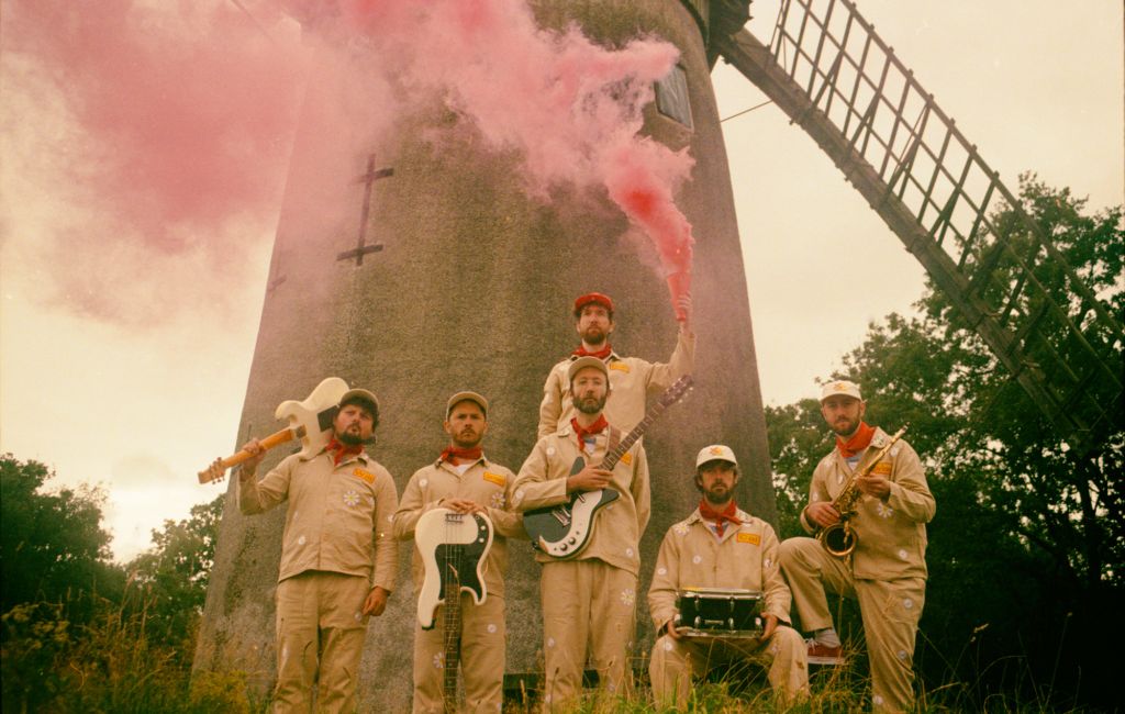 Melin Melyn dressed in uniforms and with their instruments in front of a windmill, photo by Claire Marie Bailey