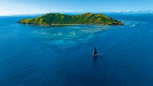 Aerial shot of a yacht in a vast expanse of blue sea with an island behind