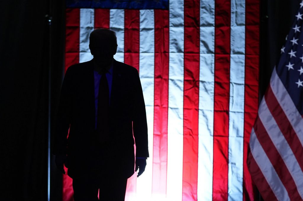 Donald Trump, darkly silhouetted against American flags