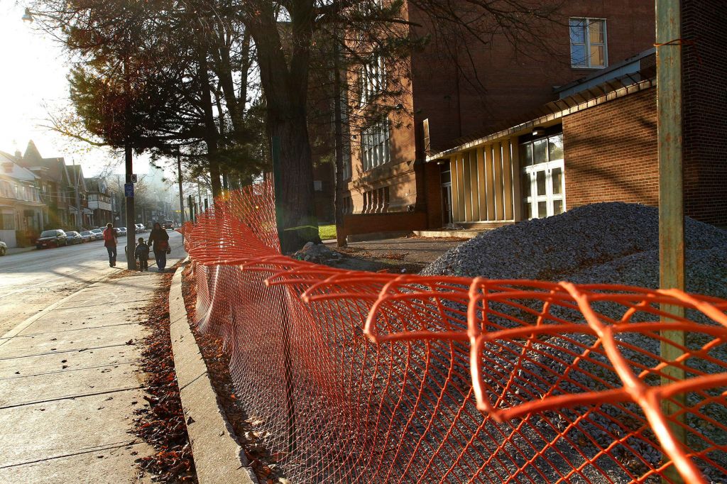 A school separated by a sidewalk with an orange fence and pile of gravel.