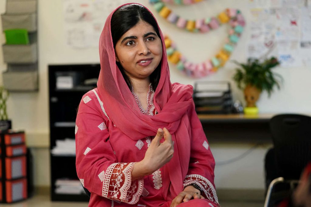 Malala Yousafzai, wearing a deep pink dress and head scarf, gestures while speaking to someone off camera