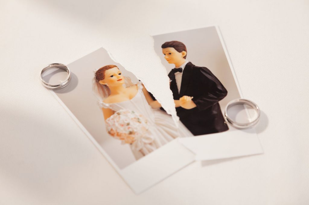 A photo of a vintage bridge and groom cake topper, ripped in half. Two rings are on separate corners of the picture.