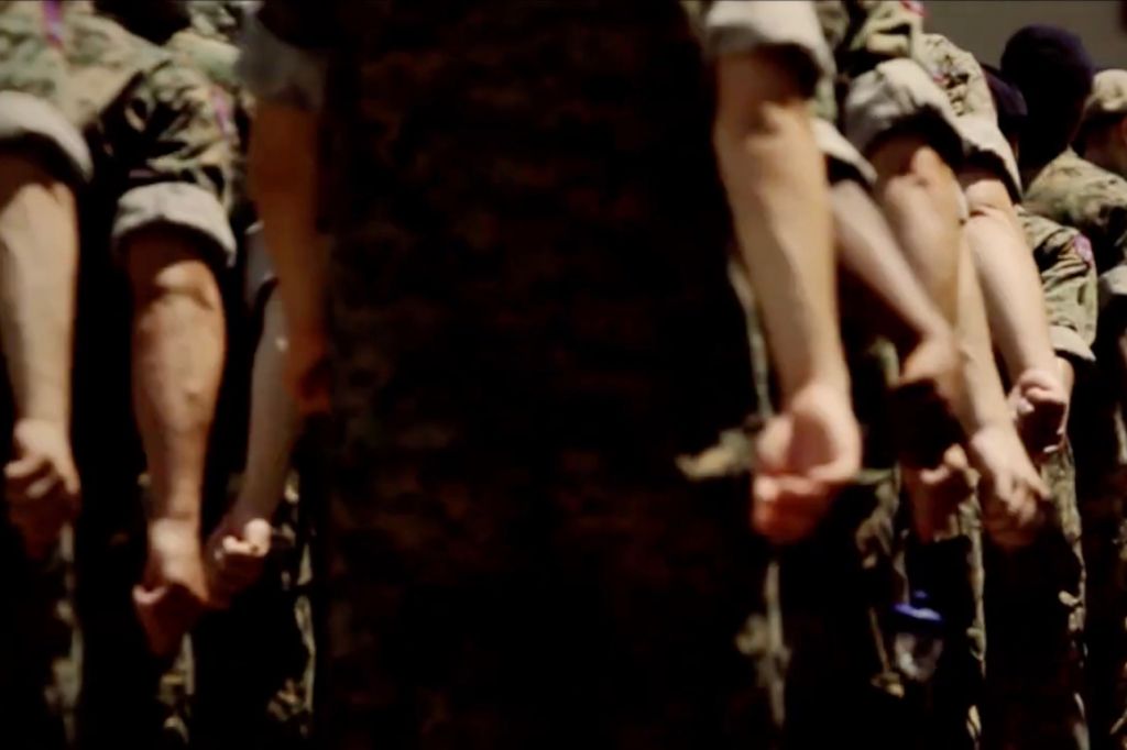 A group of boys dressed in green, short-sleeved fatigues are pictured from behind