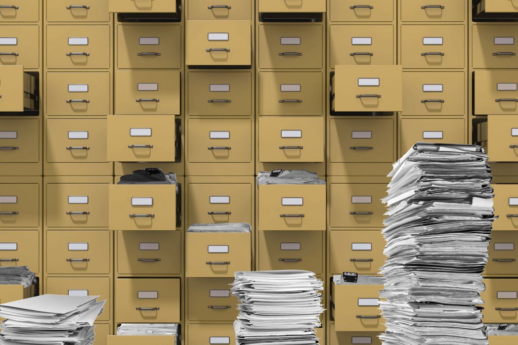 In a photo illustration, rows of yellow filing cabinets with several drawers open. Several stacks of papers are in the foreground.