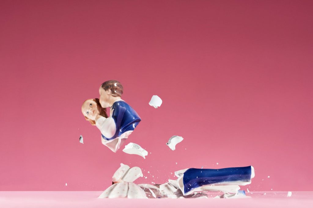 A vintage statue of a man kissing a woman is smashed to pieces against a bright pink background