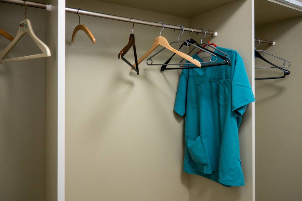 in a photo, green scrubs hang in a closet with several empty, askew coat hangers