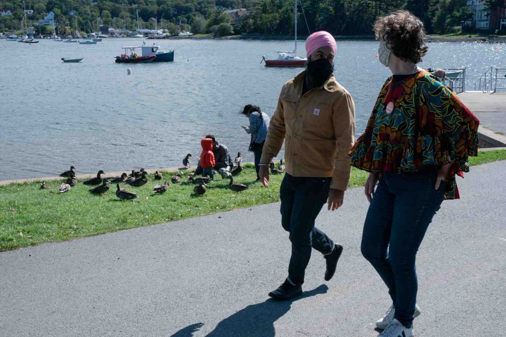 Jagmeet Singh and Lisa Roberts walk along a waterfront path. A child and adults are in the background looking at ducks