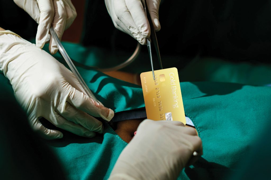 A photo illustration showing a person lying down in green surgical srubs. Several hands holding surgical instruments appear to be pulling a gold credit card from their body