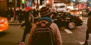 A woman with a backpack crossing a busy city street at night.