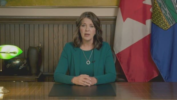 Premier Danielle Smith sits at a desk and announces her government's plan to build schools. 