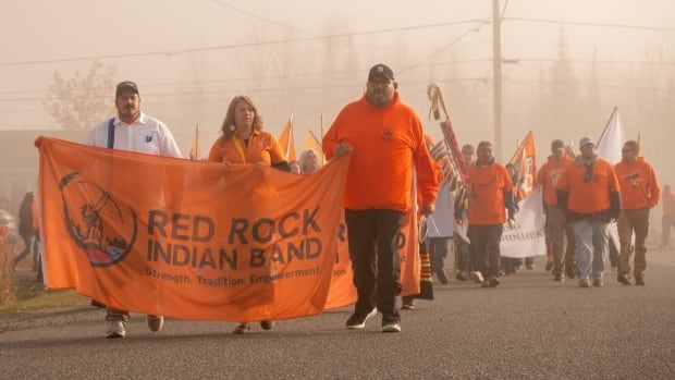 A large group of people dressed mostly in orange walk along a foggy road.