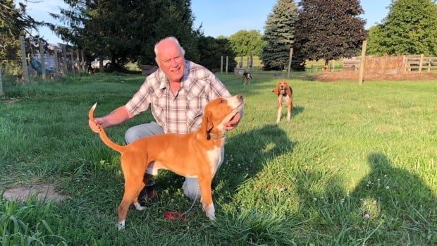 A man poses with a dog, holding its tail and chin