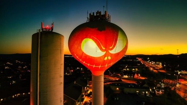 A smirking cartoon of a pumpkin projected on a watertower