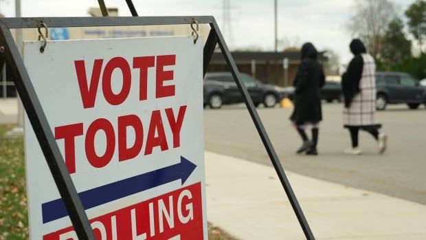 A sign that says Vote Today Polling Place with two people in the distance walking into a building