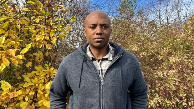 A man stands in front of some greenery .