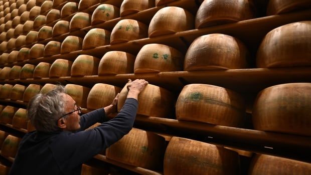 A man reaches for wheels of cheese loaded on  shelves