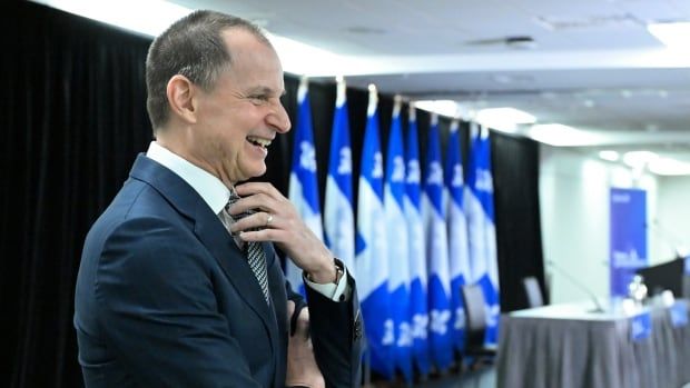 Man in suit smiles with Quebec blue and white flags behind him.